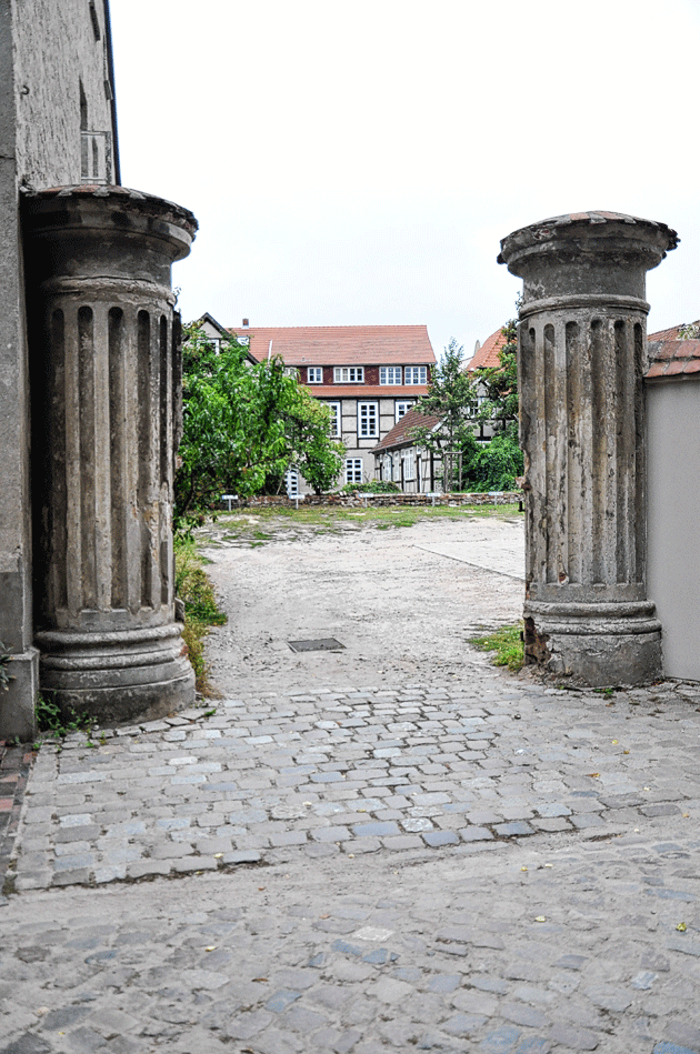 Schulstraße 6: Die Zufahrt ist unbefestigt. Die  Torpfeiler aus kannelierten Säulen sowie einem aufwendigen Kapitell werden saniert.