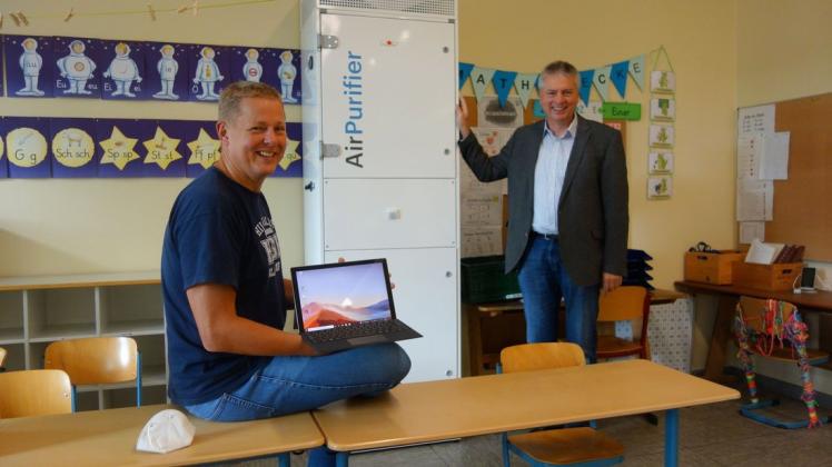 Rechtzeitig vor Schulbeginn steht der Luftfilter: Bürgermeister Herwig Wöbse hat ihn bestell, Lehrer Woldemar Schilberg (links) bezeichnete ihn scherzhaft als Kühlschrank. Auf seinem Schoß zeigt er seinen neuen Laptop.