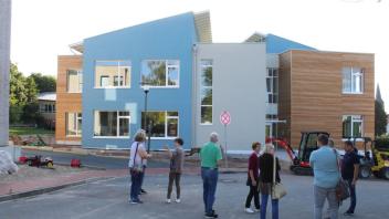 Mitglieder des Ausschusses für Gebäudemanagement der Gemeinde Lotte besichtigen die in Erdfarbe gehaltene und doch bunte Außenansicht der Grundschule in Alt-Lotte von der Hambrinkstraße aus.