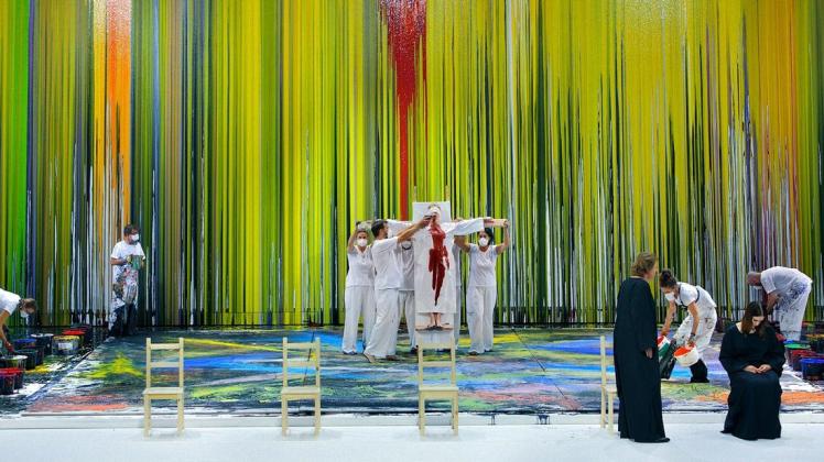 Jemand wird gekreuzigt, einige bemalen Boden und Wände mit dicker Farbe, und vorne sitzen Siegmund (Klaus Florian Vogt, vorne links) und Sieglinde (Lise Davidsen) - so sieht es aus, wenn Hermann Nitsch "Die Walküre" in Bayreuth bebildern darf.