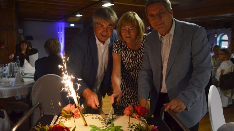 Bürgermeister Oliver Hermann, Birgit Runge und Karsten Korup (v. r.) schneiden die Geburtstagstorte an.