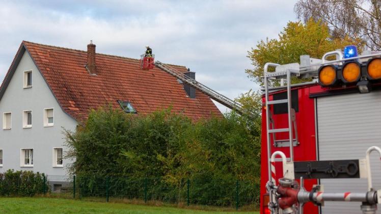 Ein Feuerwehrmann kontrolliert auf einer Drehleiter den Schornstein eines Wohnhauses.