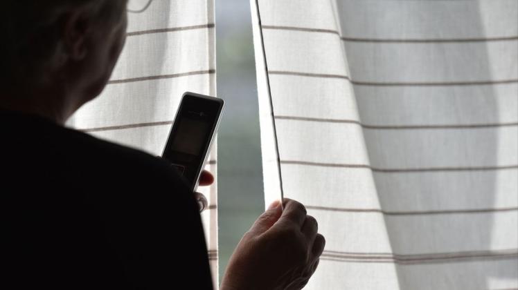 Angst vor dem Stalker: Eine Frau steht mit Telefon  am Fenster.
