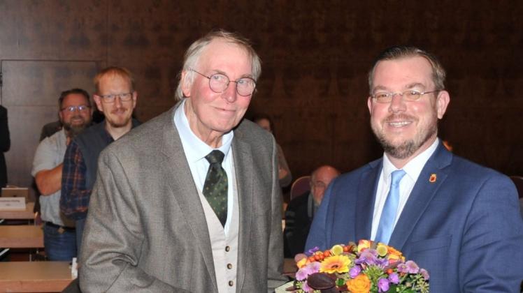 Ratsvorsitzender Friedhelm Führs (l.) überreicht Jan Peter Bechtluft zum Abschied nach 15 Jahren als Bürgermeister Blumen, die allermeisten Ratsmitglieder applaudieren im Stehen.