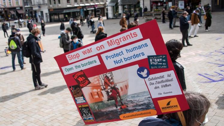 Eine Teilnehmerin einer Kundgebung gegen die Abschiebehaftanstalt in Glückstadt steht auf dem Gänsemarkt und hält ein Plakat mit der Aufschrift „Stop war on Migrants“.