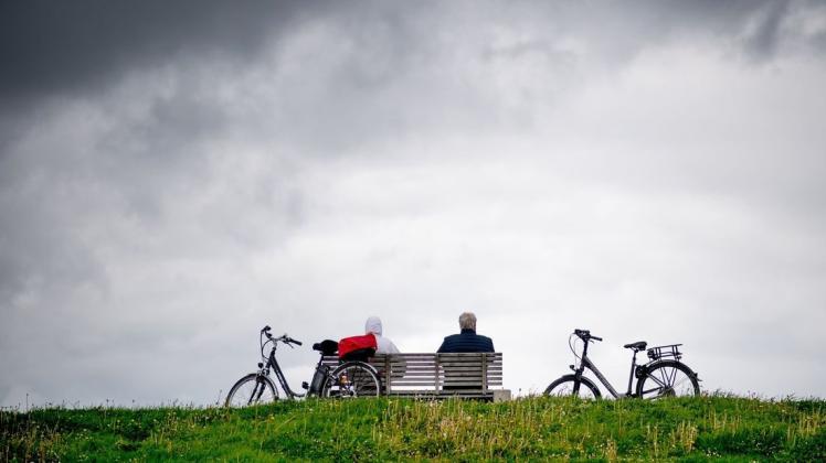 Touristen sitzen vor dunklen Wolken auf einer Bank auf dem Deich und genießen ihre Pause.
