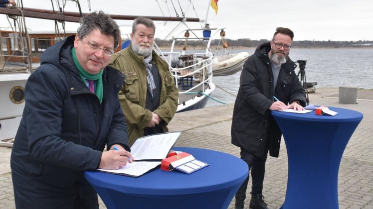 Finanzminister Reinhard Meyer (SPD, l.) und Oberbürgermeister Claus Ruhe Madsen (parteilos, r.) unterzeichneten im Beisein von Landtagsabgeordneten Ralf Mucha (SPD) eine Vereinbarung für das Archäologische Landesmuseum in Rostock.