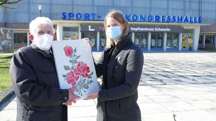 Blumen sollen Mut spenden: Schweriner Heinz Kolbe überreicht ein selbst gebasteltes Mosaik an Cathrin Richter, die für die Organisation des Impfzentrums zuständig ist.