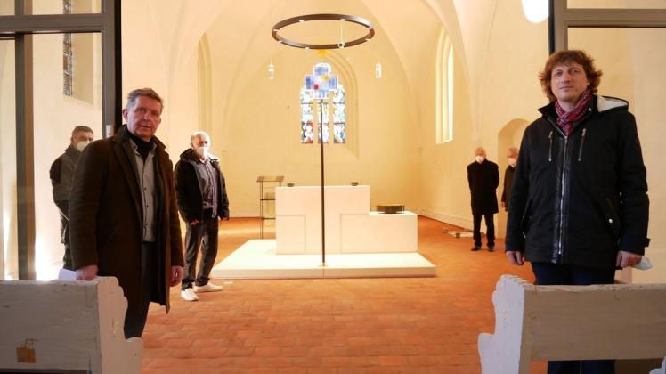 Der neue Altarraum der Kirche in Blankenhagen lockt mit neuer Farbe und hellem Glaskreuz. Architekt Matthias Schmidt (vorne links) und Pastor Stefan Haack (rechts) stehen an der verschiebbaren Glastür, die im Winter vor der Kälte schützen soll.
