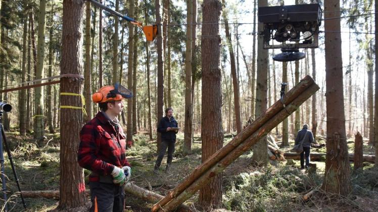Auf Knopfdruck kann Marc Hinz (links) die runden Baumstämme per Laufkatze die rund 130 Meter durch den Wald zum Ablageplatz transportieren. Prof. Dr. Dr. Michael Mussog untersucht den Einsatz wissenschaftlich.