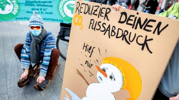 Ein Teilnehmer sitzt während einer Demonstration von Fridays for Future neben einem Plakat mit der Aufschrift "Reduzier deinen Fussabdruck" auf einem Schlitten, um auf die Folgen des Folgen des Klimawandels hinzuweisen.