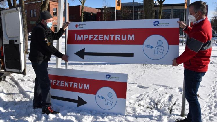 Ein fester Halt soll noch folgen: Klaus Huntemann (links) und Rotkreuz-Chef Michael Pleus platzieren die neuen Hinweisschilder an der schmalen Straße zum Impfzentrum.