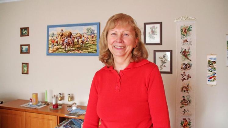 Sie  liebt das Sticken in ihrer Freizeit: Hier steht Marion Hanika aus Tarnow zwischen ihrem Lieblingsbild, dem blaugerahmten Erntebild, und dem Glockenstrang mit vielen Tieren aus der Natur.