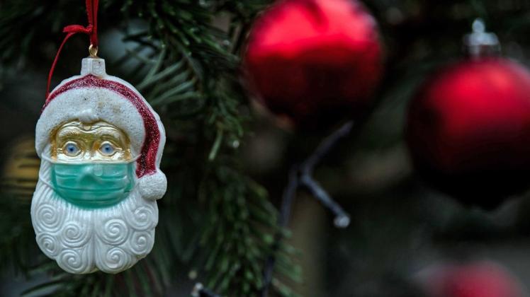 Ein Weihnachtsmann mit einer Schutzmaske hängt als Weihnachtsbaumschmuck in einem Tannenbaum. (Symbolfoto)