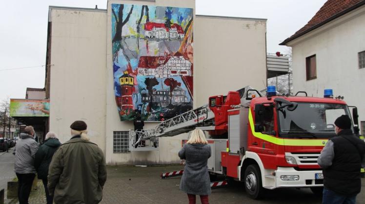 Ungewöhnlicher Einsatz für die Drehleiter der Feuerwehr Dissen: Sie half dabei, das Gemälde von Wolfgang Meluhn an seinen Platz in der Großen Straße zu hängen.