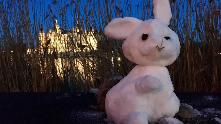 Ein kleiner Schneehase sitzt auf der Burgseepromenade vor dem Schweriner Schloss. Der Erbauer ist unbekannt.