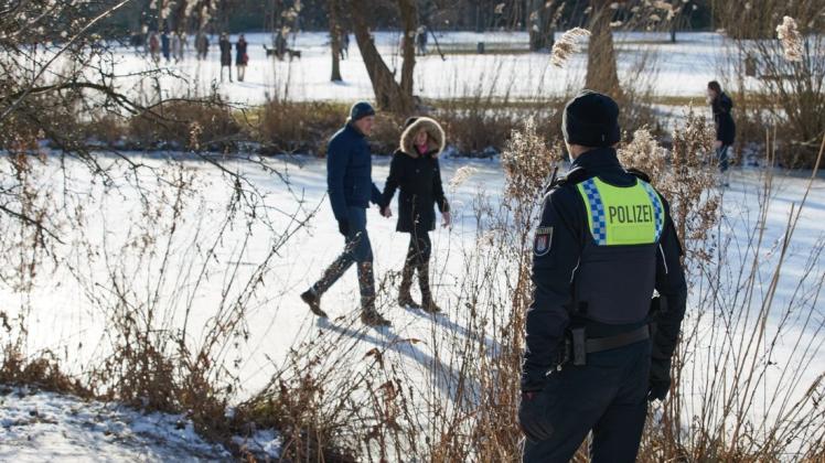 Ein Polizist ruft ein Pärchen von der Eisfläche runter, die auf einem Gewässer im Alsterpark an der Außenalster spazieren gehen. Das Betreten von Eisflächen ist in Hamburg untersagt.
