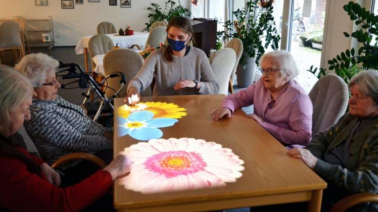 Mit den Händen können die Senioren die Projektionen auf dem Tisch bewegen. Aurelia Gryczka unterstützt sie dabei.