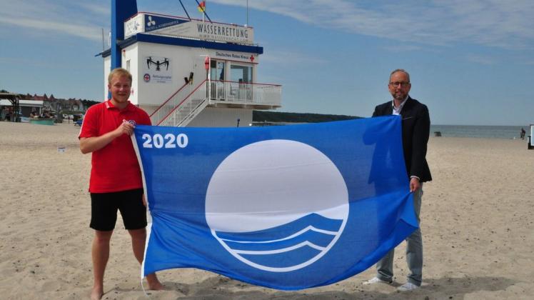 Zum 23. Mal hat Warnemünde die Blaue Flagge erhalten: Stolz zeigen Tourismusdirektor Matthias Fromm und Eike Reck von der DRK-Wasserwacht das neue Exemplar.