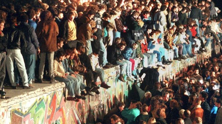9. November,1989, Berlin: Jubelnde Menschen sitzen mit Wunderkerzen auf der Berliner Mauer.