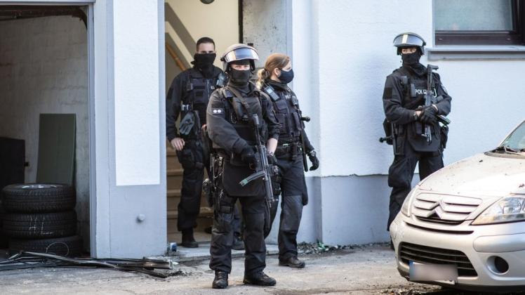 Schwer bewaffnete Polizeibeamte stehen vor einem Wohnhaus, das bei einer Razzia gegen Clankriminalität durchsucht worden ist.