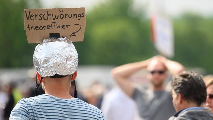 Ein Demonstrant trägt einen Aluhut mit einem Schild, auf dem "Verschwörungstheoretiker" steht.
