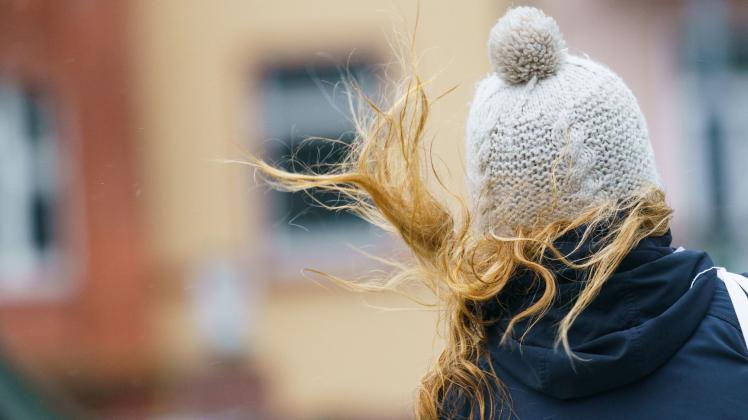 Ein Frau draußen mit Mütze und fliegenden Haaren von hinten.