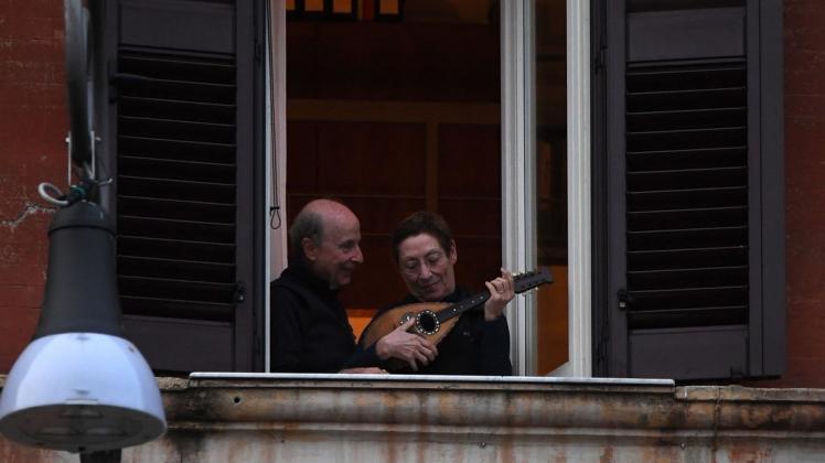 Trost in trister Corona-Zeit: Ein Mann und eine Frau mit einem Instrument stehen an einem geöffneten Fenster, und nehmen am «Flashmob sonoro» (klingender Flashmob) in Italien teil. Foto: Elisa Lingria/XinHua/dpa
