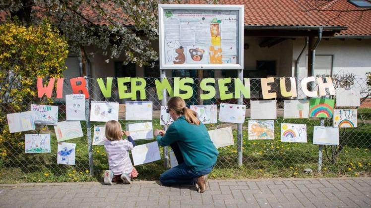 Eine Mutter befestigt mit ihrer Tochter ein selbstgemaltes Bild am Zaun eines geschlossenen Kindergartens in der Region Hannover. Die Kitas bleiben bis auf die Notbetreuung weiterhin geschlossen. Foto: dpa