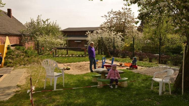 Viel Platz: Erzieherin  Astrid Fischer mit Kindern aus ihrer Gruppe auf dem Spielplatz, eingeteilt durch Absperrband. Auch die anderen Gruppen haben Sand, Sitze und Rutsche.