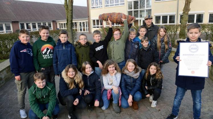 So sehen Rekordhalter aus: Die frühere Klasse vier der Overbergschule Voltlage hat mit ihrem 1,1 Kilometer langen Freundschaftsband aus mehr als 150.000 Gummibändern in Deutschland eine Bestmarke geschafft. Stolz präsentieren die Jungen und Mädchen zusammen mit ihrem früheren Klassenlehrer Lutz Dalkowski die Urkunde. Foto: Christian Geers