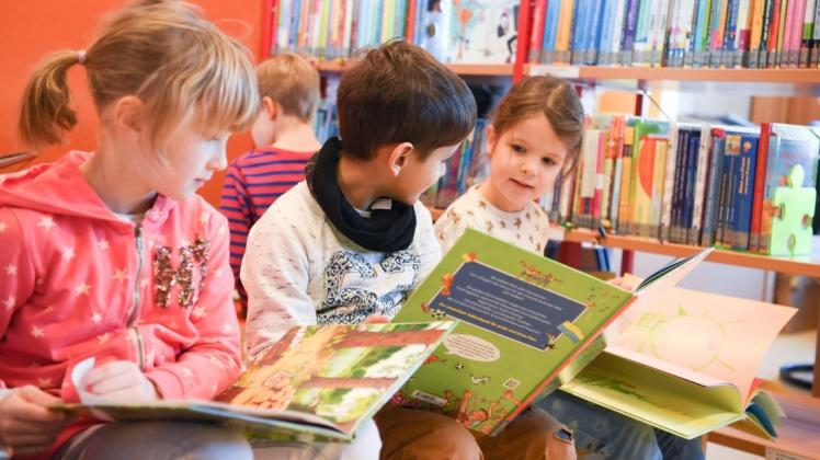Zwei Schülerinen und ein Schüler der Klasse 1/2 lesen in einer Schulbibliothek. Foto: Arne Dedert/dpa