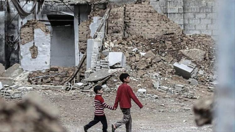 Zwei syrische Jungen gehen Hand in Hand an zerstörten Häusern vorbei. 