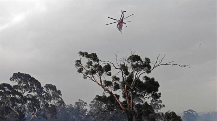 Ein Löschhubschrauber fliegt über Bäume vor rauchverhangenem Himmel im Vorort Bundoora von Melbourne. 
