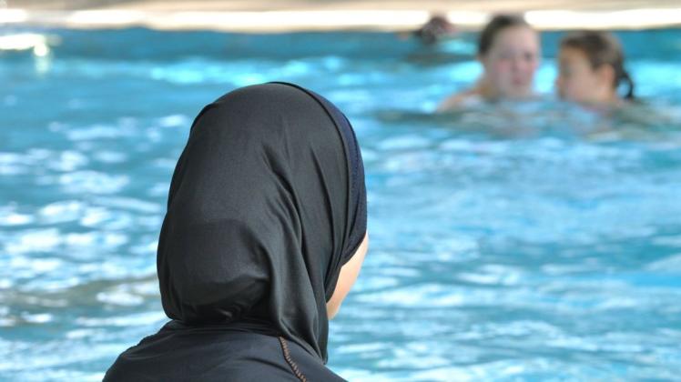 Eine muslimische Schülerin sitzt in einem Burkini am Rande eines Schwimmbeckens. Foto: dpa/Rolf Haid