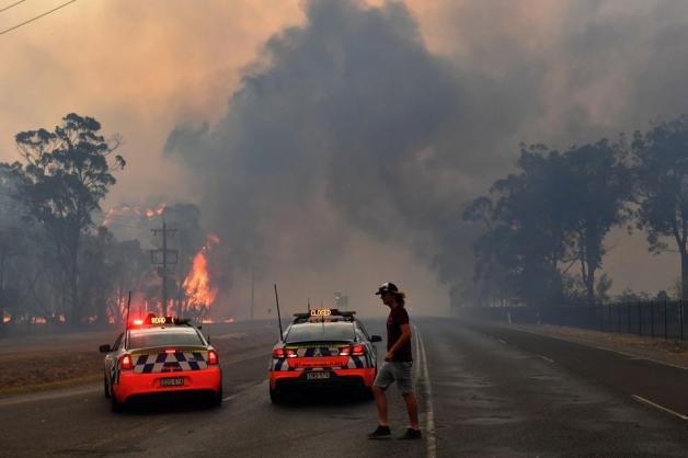 19.12.2019: Die Polizei sperrt mit zwei Polizeiautos südwestlich von Sydney eine Straße zu einem Gebiet, das in Flammen steht. 19.12.2019: Die Polizei sperrt mit zwei Polizeiautos südwestlich von Sydney eine Straße zu einem Gebiet, das in Flammen steht.