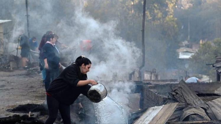 Einwohner schütten Wasser auf die qualmenden Überreste ihrer Häuser, die bei einem Brand zerstört wurden. 