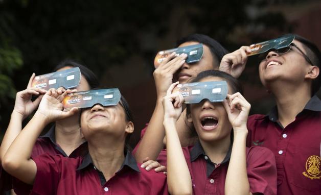 Schüler in Bangkok (Thailand) halten Schutzbrillen vor den Augen, um die Sonnenfinsternis zu beobachten. Foto: dpa/Sakchai Lalit/AP
