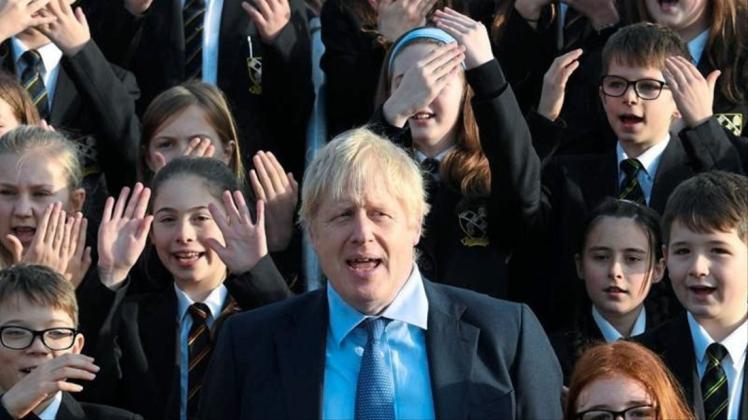 Großbritanniens Premierminister Boris Johnson (M) steht zwischen Schüler bei seinem Besuch eines Colleges. 