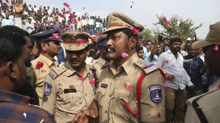 Menschen werfen Blütenblätter auf indische Polizisten. Foto: dpa/Mahesh Kumar A