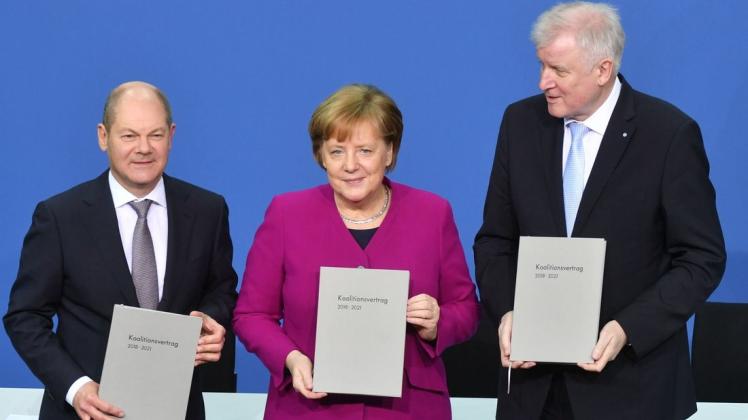 Bundeskanzlerin Angela Merkel (CDU), der CSU-Vorsitzende Horst Seehofer (r) und der kommissarische SPD-Vorsitzende Olaf Scholz halten nach der Unterzeichnung im Paul-Löbe-Haus den Koalitionsvertrag. Foto: dpa/Bernd von Jutrczenka