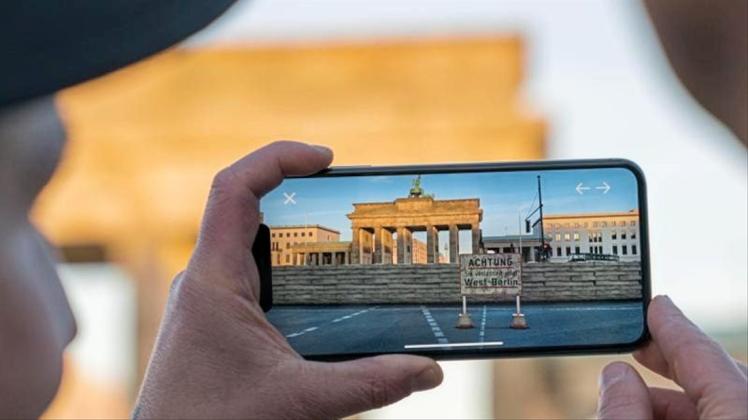 Apple-Chef Tim Cook lässt sich am Brandenburger Tor von Entwickler Peter Kolski das Projekt „MauAR“ auf einem Smartphone erklären. 