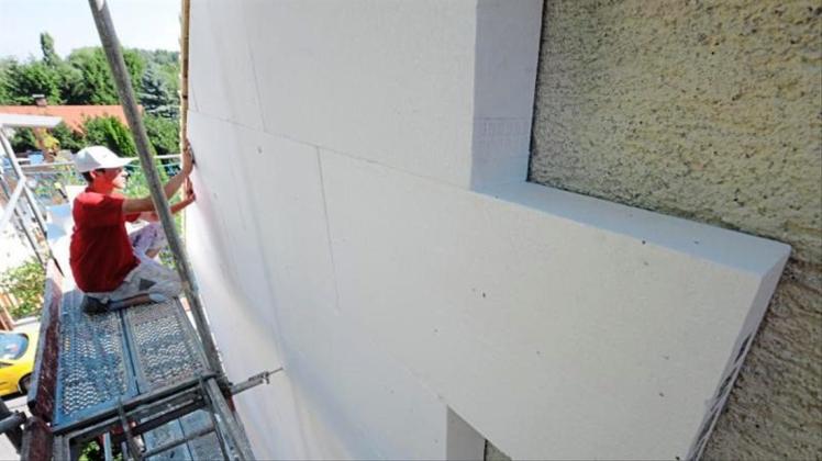 Ein Arbeiter befestigt Styroporplatten zur Wärmedämmung an einer Hausfassade. 