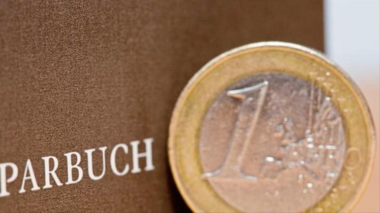 Eine Ein-Euro-Münze steht neben einem Sparbuch. 