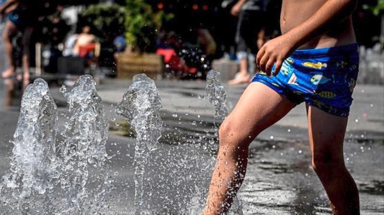 Ein Kind kühlt sich in einem Springbrunnen ab. In Deutschland wird es heiß. 