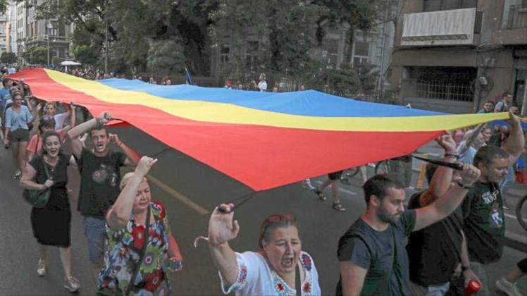 Menschen halten eine rumänische Flagge während einer Demonstration zum Gedenken an ein getötetes 15-jähriges Mädchen in Bukarest. 