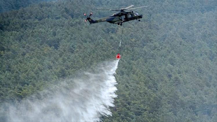 Ein Hubschrauber der Bundeswehr vom Typ NH90 mit einem Löschwasser-Behälter wirft über einer Brandstelle Löschwasser ab. 