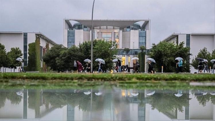 Kühl und grau: Eine Gruppe mit Regenschirmen geht am Bundeskanzleramt vorbei. 