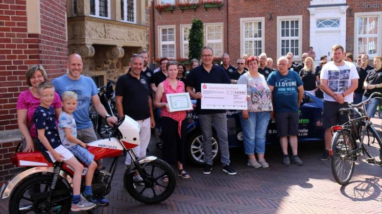 Bürgermeister Helmut Knurbein (Mitte) und der Vorsitzende der „Kult-Blech-Szene“, Guido Zepmeisel ( 5. v. links ) übergaben den Spendenscheck an die Vertreterin der „Elterninitiative Kinderkrebs Emsland“, Birgit Nee-Schawe. Über ihre Gewinne freuten sich Rolf Manning ( Herkules-Mofa ) mit seiner Familie ( links ), Jürgen Blümel ( Opel Tigra ) mit seiner Frau ( 2. v. rechts ) und Peter Schwallenberg (rechts ), der ein Miele Fahrrad aus den 1950er-Jahren gewann.  