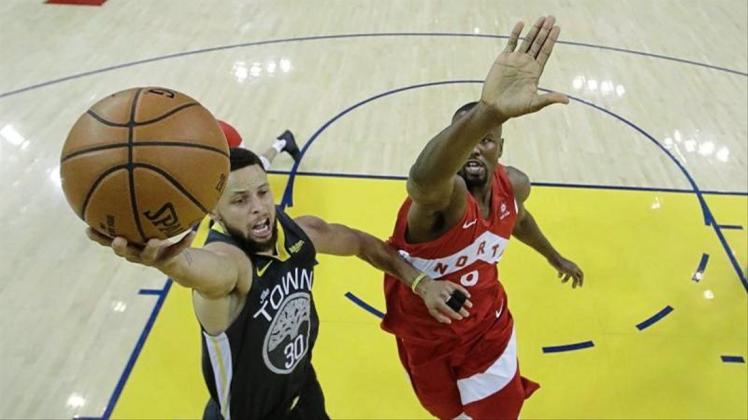 Stephen Curry (l) von den Golden State Warriors verteidigt am Korb gegen Serge Ibaka von den Toronto Raptors. 